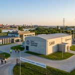 Wizualizacja kompleksu małych reaktorów jądrowych (SMR) w Polsce, z widocznym budynkiem reaktora BWRX-300 i infrastrukturą przesyłową na tle rzeki i miasta.